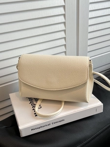 Sac bandoulière élégant en cuir grainé blanc cassé posé sur un livre avec rabat chic