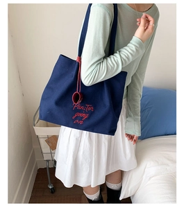 Detail showing navy canvas tote bag with red script embroidery and circular charm