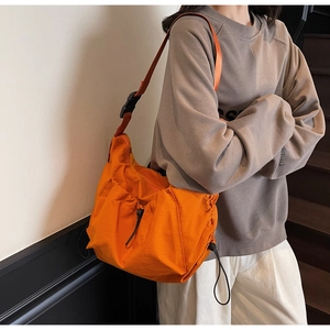 Side view of bright orange nylon crossbody bag with functional drawstring detail and strap