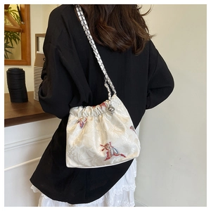Detail of floral embroidery and woven chain strap on the ivory canvas shoulder bag