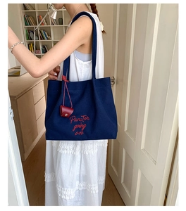 Detail of navy canvas tote bag with red embroidery lettering and leather tag accessory