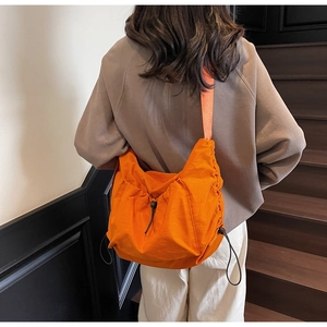 Detailed back view of a large orange nylon crossbody bag with drawstring design and wide strap