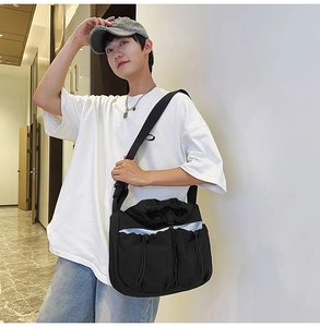 Detail of black utilitarian crossbody bag with drawstring pockets on male model
