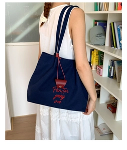 Detail of dark blue canvas tote bag featuring red floral embroidery and leather charm
