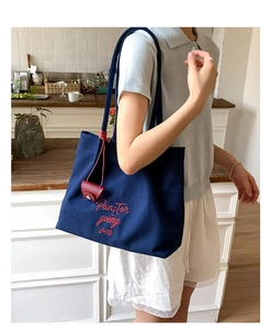 Detail of embroidered navy canvas tote bag with red script and leather pendant
