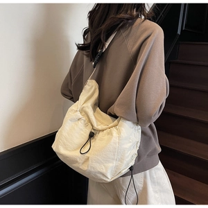 Detail view of large cream crossbody tote bag with side drawstring and black buckle strap