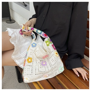 Detail einer gestrickten Tote-Bag im Lazy-Stil mit bunten 3D-Häkelblumen auf Holzbank