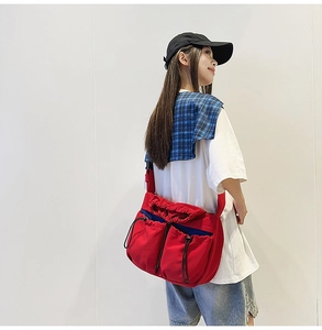 Detail view of large red pleated crossbody bag with drawstring pockets and blue trim