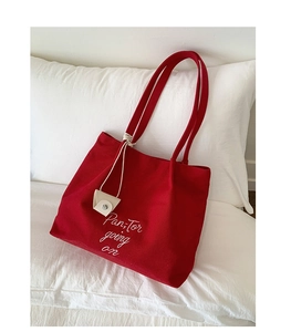 Detail of red canvas tote bag with elegant white embroidery on white pillow background
