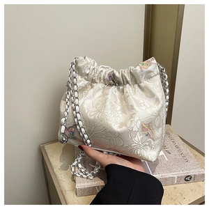 Detailed close-up of vintage floral embroidery and silver chain on beige canvas handbag