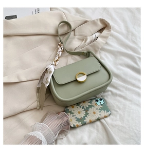 Détail d'un sac selle vert avec ruban de soie cerise et boucle dorée sur un blazer