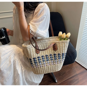 Détail du sac cabas en paille avec motifs fleuris tissés bleus et anses en cuir marron