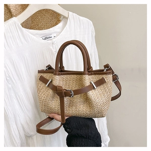 Close-up of woven straw tote bag featuring brown leather trim and silver metal buckle detail
