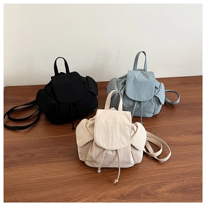Detailed view of three minimalist drawstring canvas backpacks in black, blue, and beige