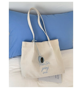 Close-up of beige canvas tote bag featuring blue embroidered letters and matching charm