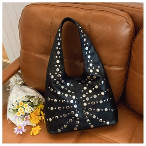 Detail of black leather hobo bag with radial silver rivet studs on a sofa