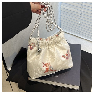 Detail of floral embroidery and drawstring closure on canvas bucket bag with metal charm