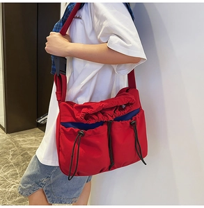 Detail of red pleated canvas crossbody bag with large front drawstring pockets and blue accents
