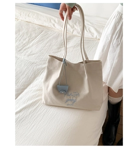 Detail of beige canvas tote bag featuring blue embroidery and a light blue pendant charm