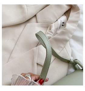 Détail de la couture d'un sac en cuir vert posé sur une veste de costume beige