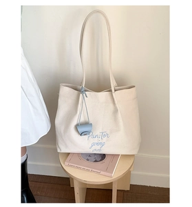 Close-up of embroidered blue text on beige canvas tote bag with mini leather charm