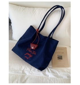 Detail of navy canvas tote bag with red embroidery and attached leather charm purse