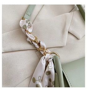 Détail de la bandoulière dorée avec foulard cerise sur un sac besace vert clair