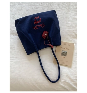 Detail of navy canvas tote bag with red Pan-Ter embroidery and leather charm accessory