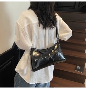 Detail of black glossy patent leather shoulder bag with V-shaped stitching and heart charm
