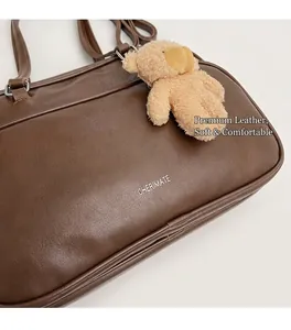 Detail view of brown leather pillow bag featuring brand text and a cute bear charm