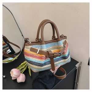 Close-up of colorful woven straw tote with brown leather handles and metal buckle detail
