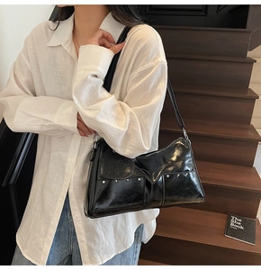 Detail of black glossy shoulder bag with silver rivets and unique V-shaped layering