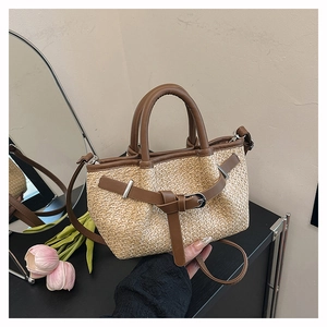 Detailed view of woven straw tote bag featuring brown leather trim and metal buckle