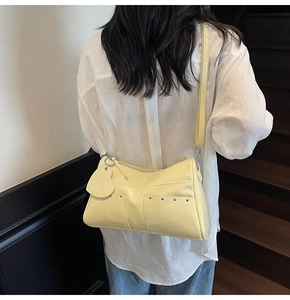 Side view of a pale yellow patent leather shoulder bag with heart charm and silver rivets