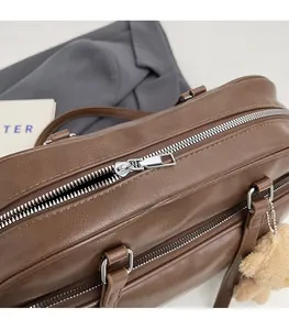 Close-up of smooth silver zipper and plush bear charm on brown leather boston bag