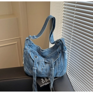 Detail view of denim crossbody bag featuring two front pockets and fringe tassels