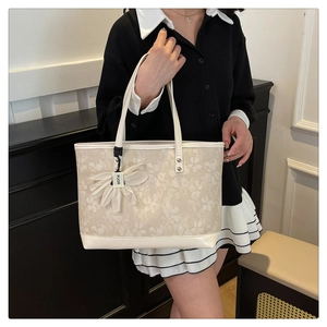 Detailed close-up of beige tote bag with floral embroidery and white flower charm pendant