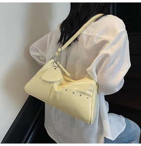 Detail of a pale yellow patent leather shoulder bag with studs and heart charm pendant