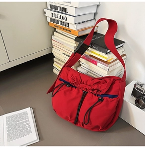 Detail of red drawstring nylon crossbody bag with dual black cords and navy lining