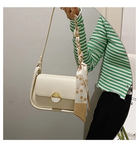 Détail du sac selle blanc cassé avec boucle dorée et ruban de soie décoratif sur la bandoulière