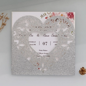 Detail of silver glitter laser-cut wedding invitation with hollow heart and floral inner card