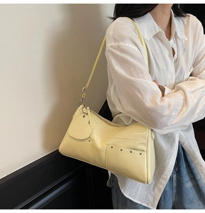 Detail of light yellow glossy leather shoulder bag with rivets and heart charm on model