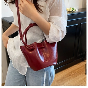Detail of dark red bucket bag with glossy pleated leather and knotted round handle