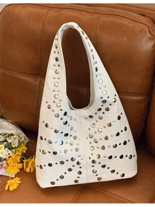 White oversized hobo bag with silver rivets on brown leather sofa and daisy floral decor
