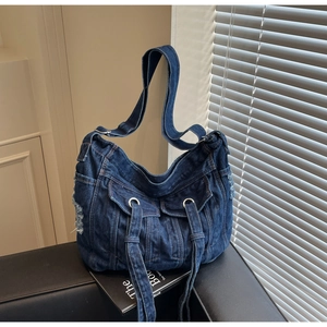 Detail of blue denim hobo bag featuring washed fringe edges and dual front pockets