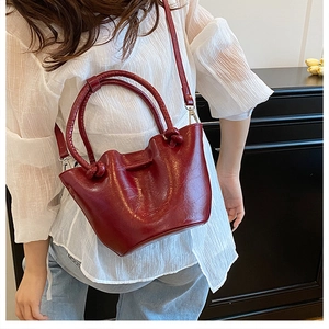 Detail of dark red bucket bag featuring a woven knot handle and textured faux leather