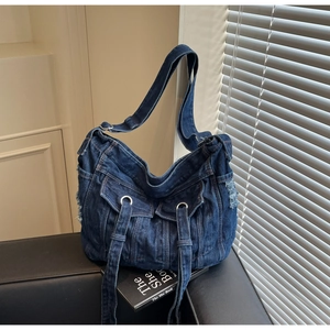 Detail of dark blue denim shoulder bag with utility pockets and distressed raw edges