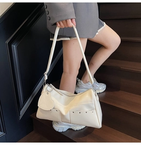 Close-up of cream glossy shoulder bag with silver rivets and heart charm on a model