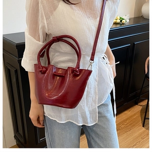 Detail view of burgundy bucket bag with round handles on model wearing white blouse