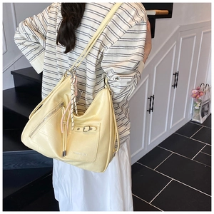 Detail view of cream yellow hobo bag featuring crocodile texture and a woven rope charm